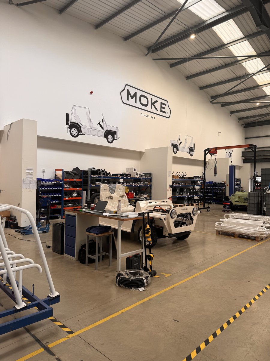 Moke factory assembly floor with organized parts station and "SINCE 1964" heritage signage